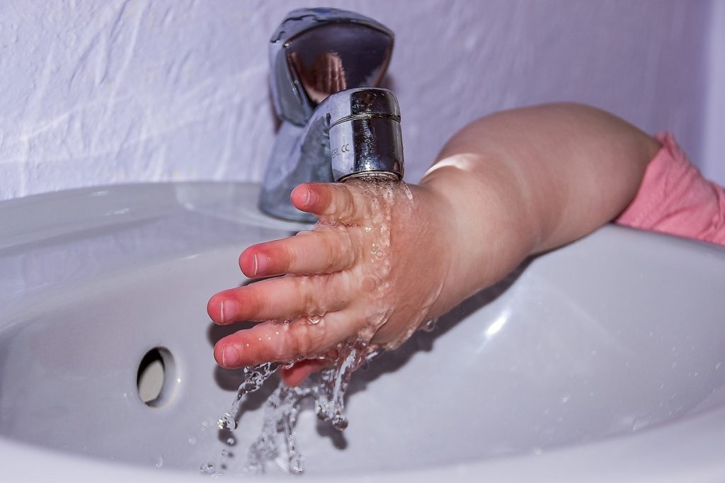 child's hand under a tap at school with what appears to be lead pipes