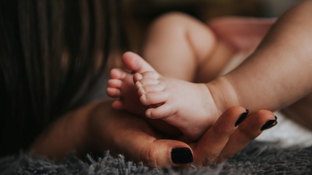 Baby's foot in women's hand, both treated with coconut oil
