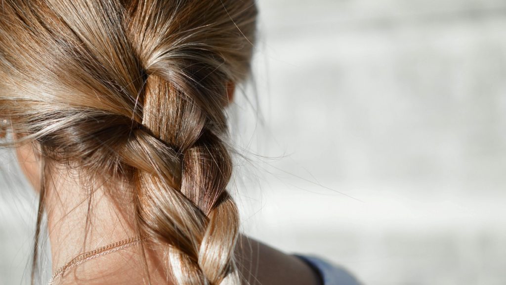 Une femme prend soin de ses cheveux blonds, tressés, avec de l'huile de coco