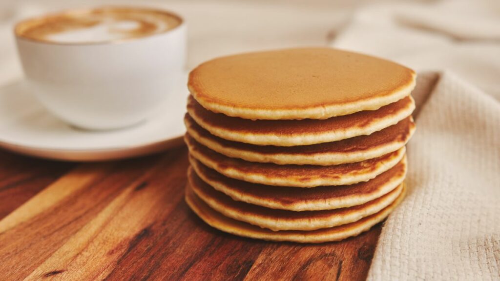 A stack of small thick pancakes and a cappuccino with date syrup